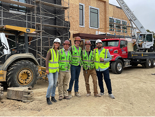 A photo of the Constructable team wearing PPE and visiing a customer at a commercial construction project job site with lots of heavy machinery in the background